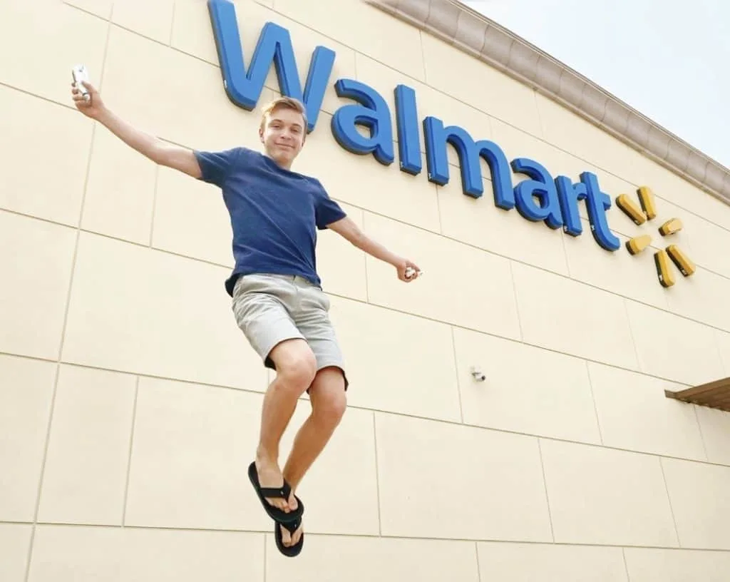 Boy jumping in front of Walmart with a Nathan's Hotdog in his hand.